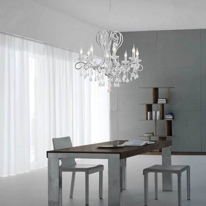Classic crystal chandelier positioned above a minimalist dining table in a bright room with sheer curtains and neutral furnishings.