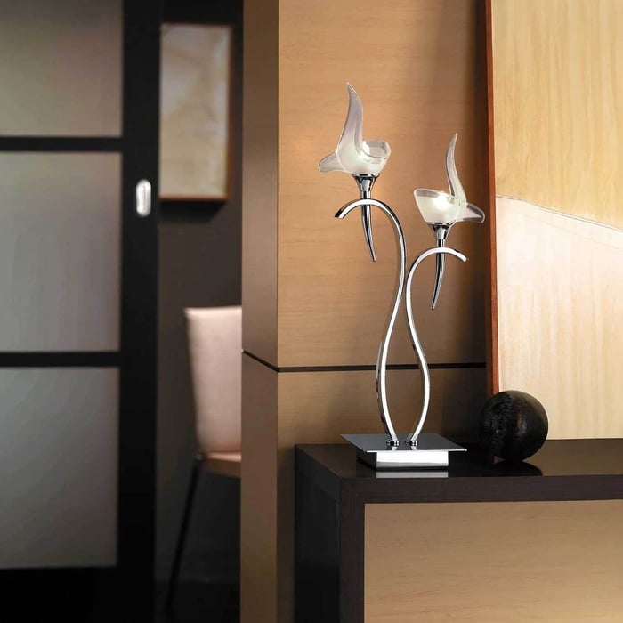 Sculptural chrome table lamp with two frosted flower-shaped shades on a console in a modern interior.