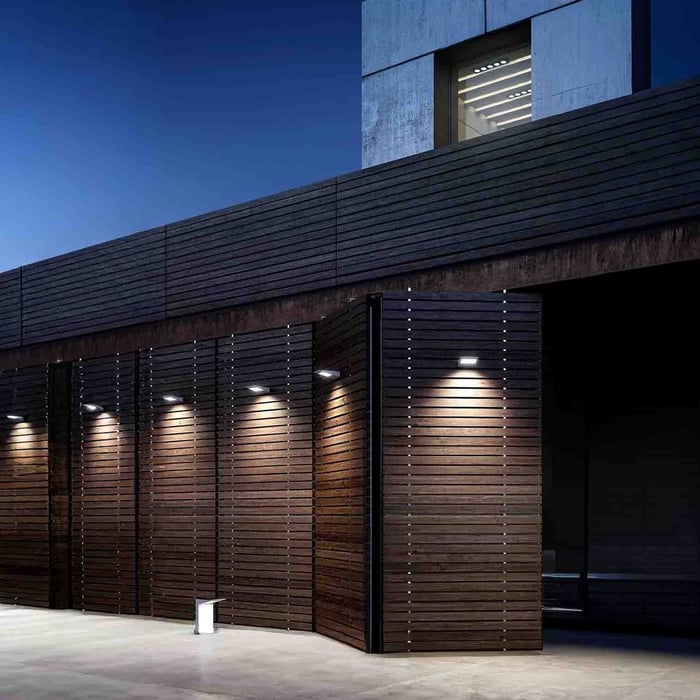 Dark brick exterior with two square outdoor wall lights illuminating a doorway and entry walkway at night.