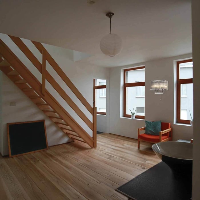 Bedroom corner with a black swing-arm wall lamp casting warm light over a bed and round bedside table.
