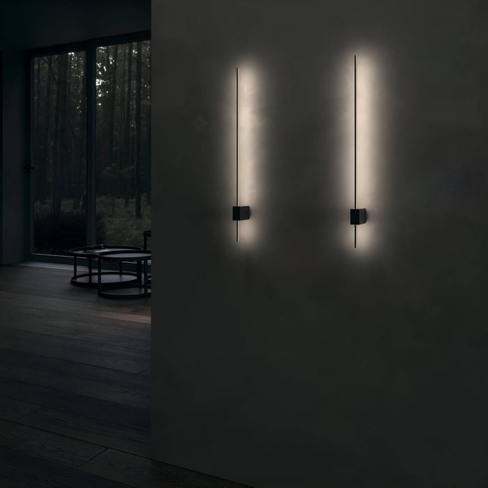 Slim, modern wall sconces casting soft vertical light on a dark wall in a contemporary space.