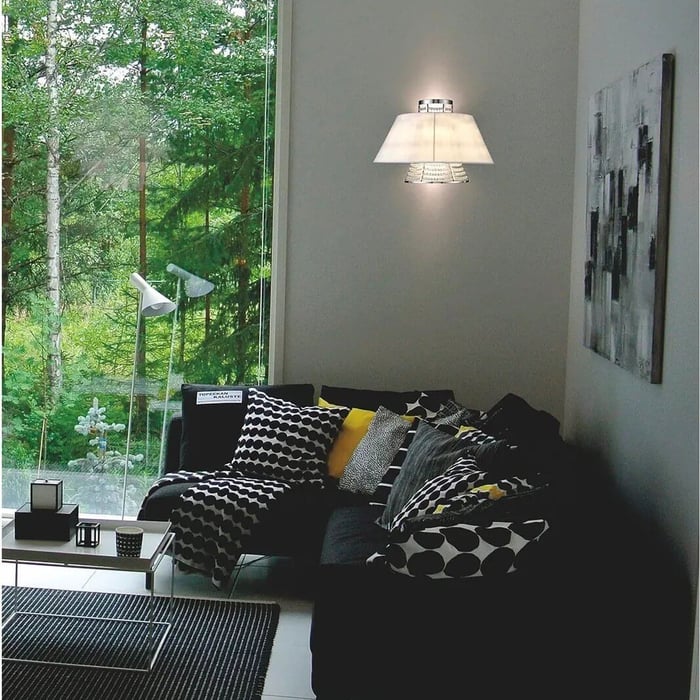 White fabric wall sconce above a black sofa with monochrome and yellow pillows in a living room with floor-to-ceiling window.