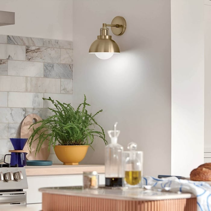 Bright kitchen corner with marble backsplash, brass dome wall sconce, potted plant, and modern accents.