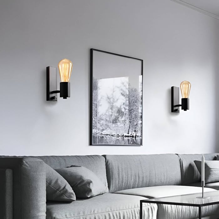 Modern black wall lights with exposed Edison bulbs above a gray sofa in a minimalist living room.