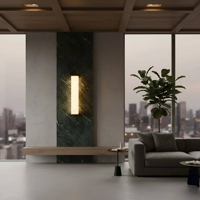 Modern apartment living room with city views, featuring a slim vertical wall sconce mounted on a dark green marble panel beside a gray sofa.