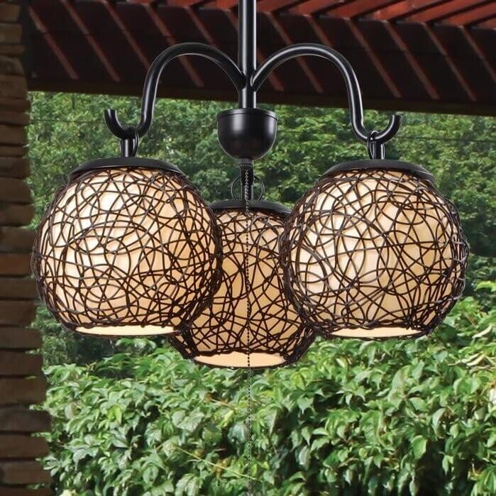 Three-light woven wicker outdoor ceiling fixture with warm glow hanging under a pergola with greenery in the background.