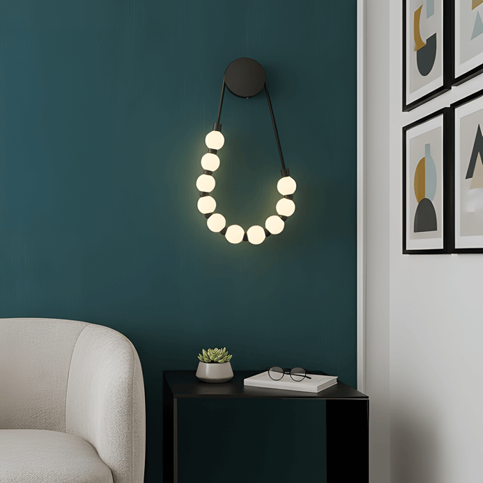 Contemporary teal wall featuring a minimalist alabaster wall light with small glowing spheres arranged in a curved drop design above a black side table.