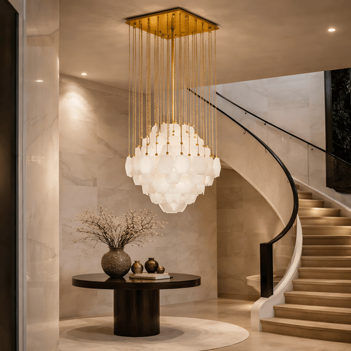 Grand staircase foyer with tiered alabaster chandelier suspended from gold ceiling mount and curved staircase backdrop.