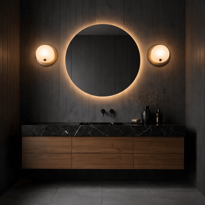 Modern bathroom vanity with round alabaster mirror and matching wall sconces on a dark wood backdrop.