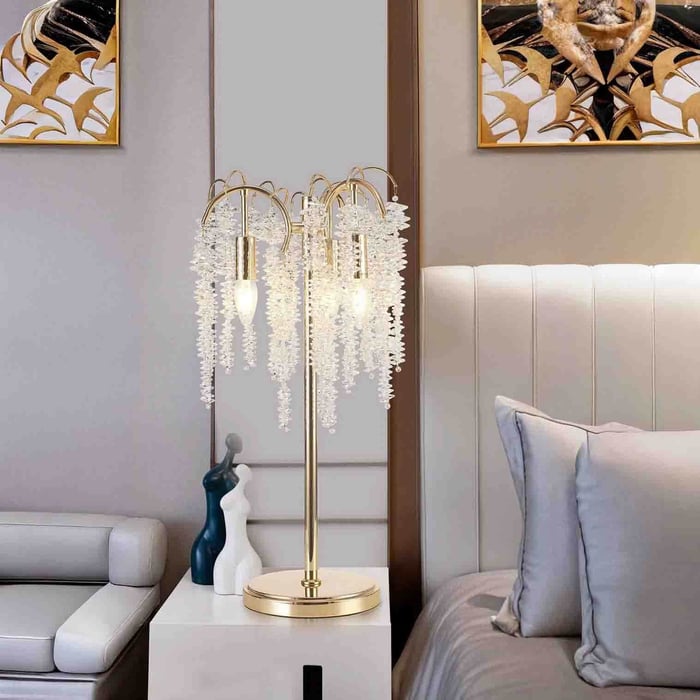 Gold table lamp with hanging crystal strands on a white bedside cabinet next to a bed and sofa.