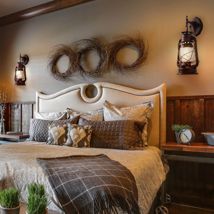 Vintage lantern-style wall sconces on either side of a bed with a tufted headboard and neutral bedding.