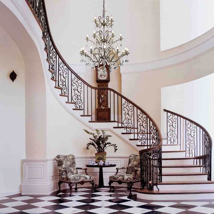 Grand multi-arm chandelier in a foyer with a curved staircase and black-and-white tiled floor.