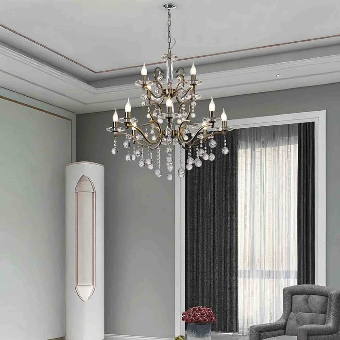 Traditional brass and crystal chandelier in a grey living room with tall curtains and a high ceiling.