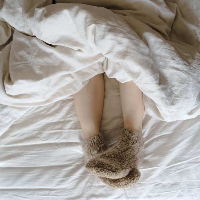 person under a blanket with warm socks, showing cold sleeper needing the best warm comforter for cold sleepers