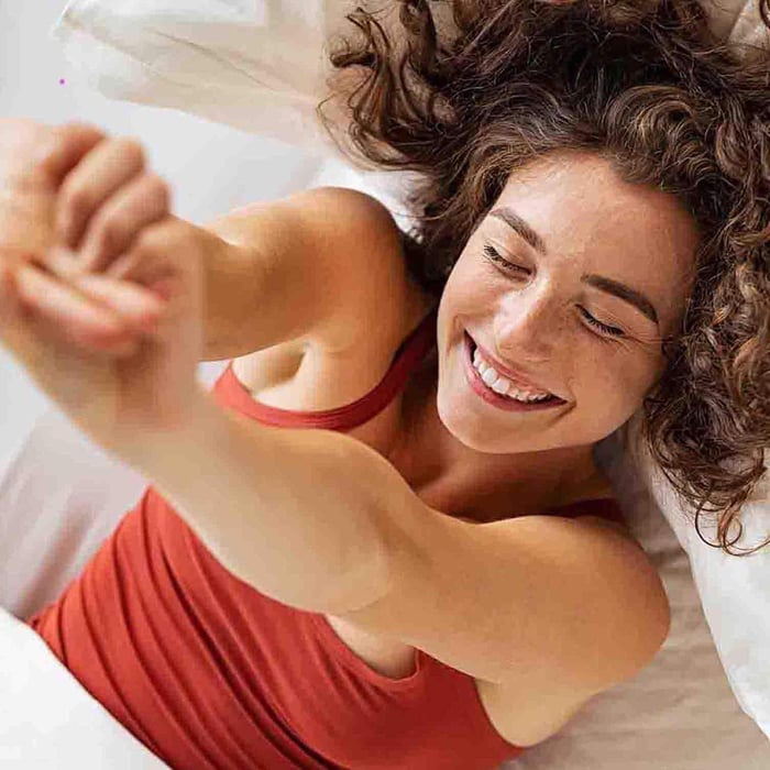 Woman waking up smiling in soft white sheets, representing the comfort and freshness of chemical-free bedding for allergy sufferers