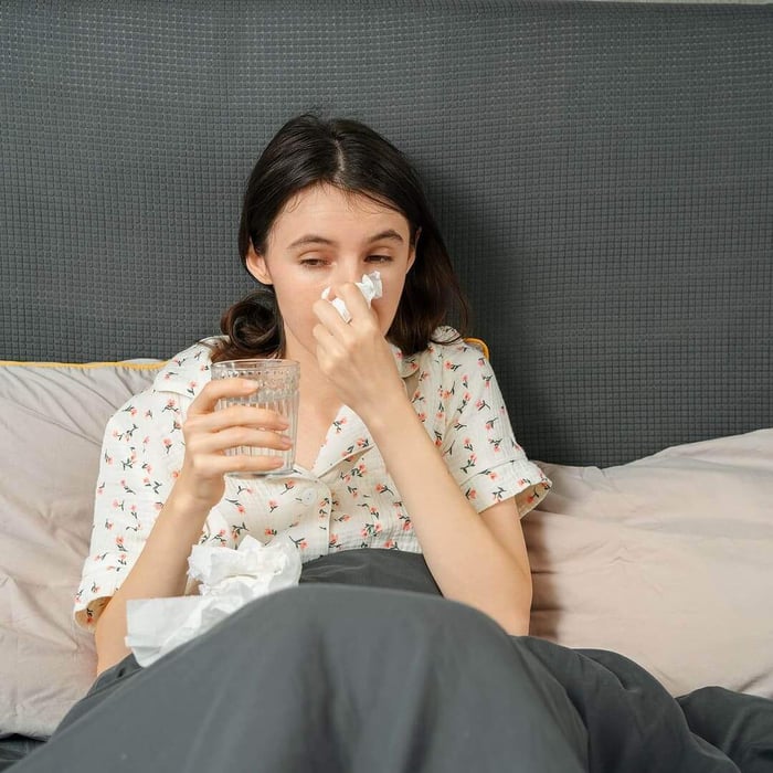 Woman experiencing down feather allergy symptoms while sitting in bed”