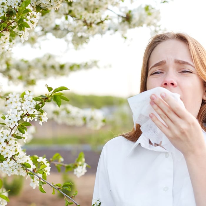 Woman sneezing outdoors, illustrating symptoms similar to goose down allergy symptoms