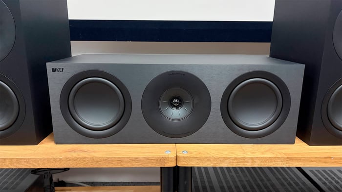 KEF Q Concerto Meta 5.1 speaker package on wood AV benches, focusing on center speaker