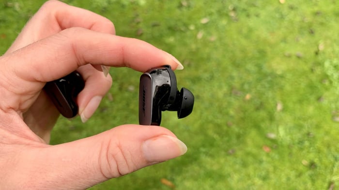 Bose QuietComfort Ultra Earbud held in hand on grassy background