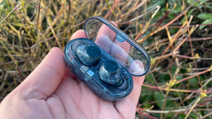 Sony WF-C710N in-ear headphones in case held in hand with bushes in background