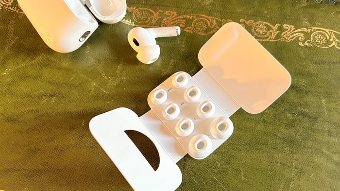 AirPods Pro 3 resting on green fabric, next to their charging case