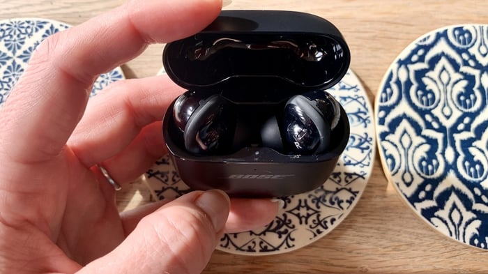 Bose QuietComfort Ultra Earbuds in case open held in hand on coffee table