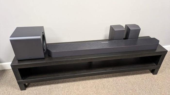 Samsung HW-Q990F soundbar, subwoofer, and rear speakers on a dark bench.