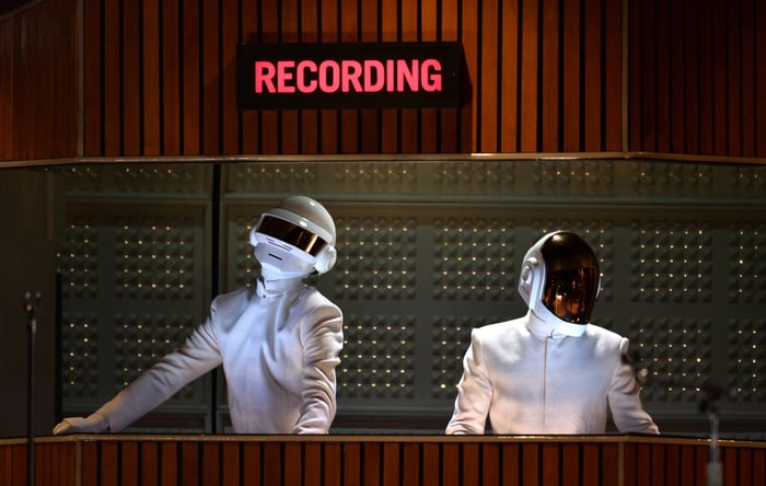 Daft Punk performing live on stage, iconic helmets shining under concert lights