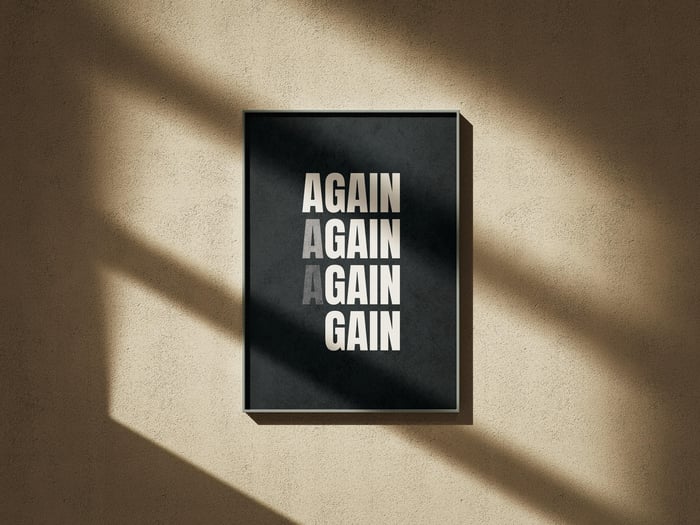 Black typography poster in a slim frame on a textured wall lit by sunlight