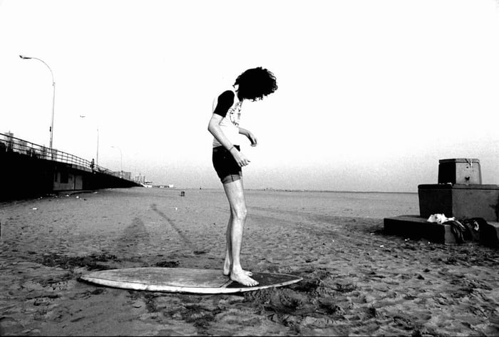 Joey Ramone standing on a surfboard at Coney Island in 1977.