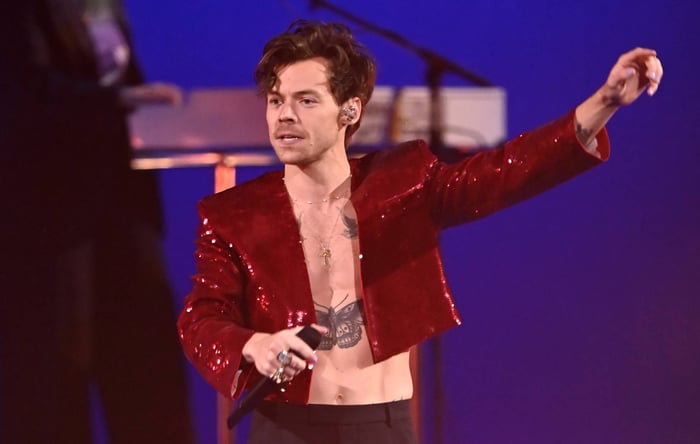Harry Styles performing on stage in 2023, dressed in a golden suit, playing piano