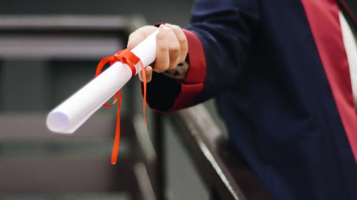 Person holding a rolled certificate tied with a red ribbon. Possible NYU project management certification.
