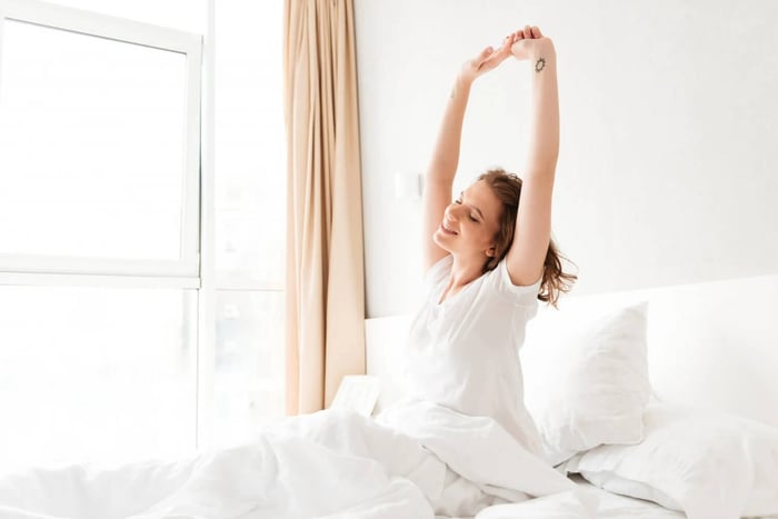 Happy woman waking up on bamboo bedding, suggesting how bamboo sheets are good for your skin and support restful sleep.