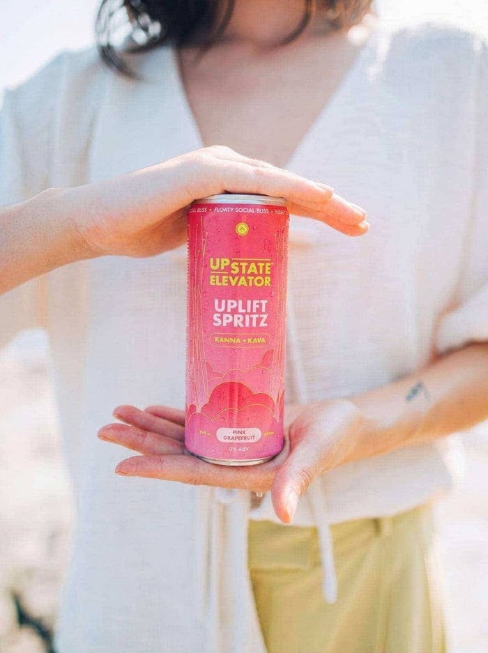 Woman in a cream shirt holding a can of Upstate Elevator Pink Grapefruit Uplift Spritz between her hands
