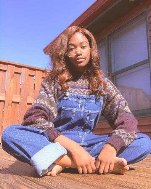 Woman sits on her porch wearing overalls and a sweater