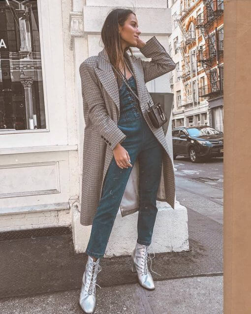 Women on a street corner wears long trench coat blazer over overalls