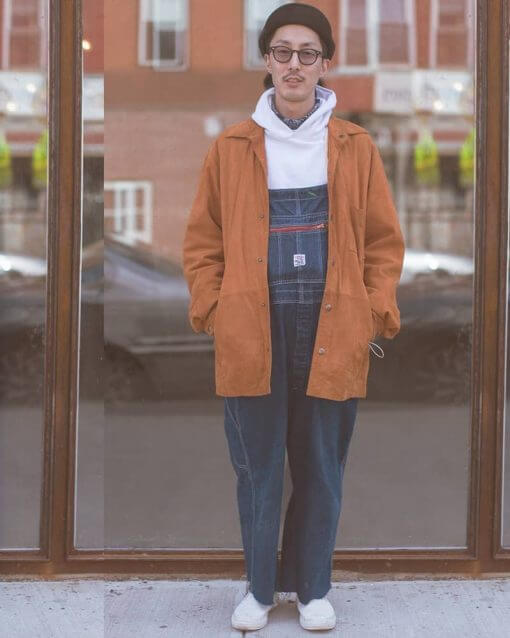 Man with hand in his pockets wears overalls.