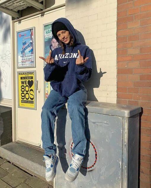 Person wearing a beanie and hooded sweatshirt while flipping a couple of birds