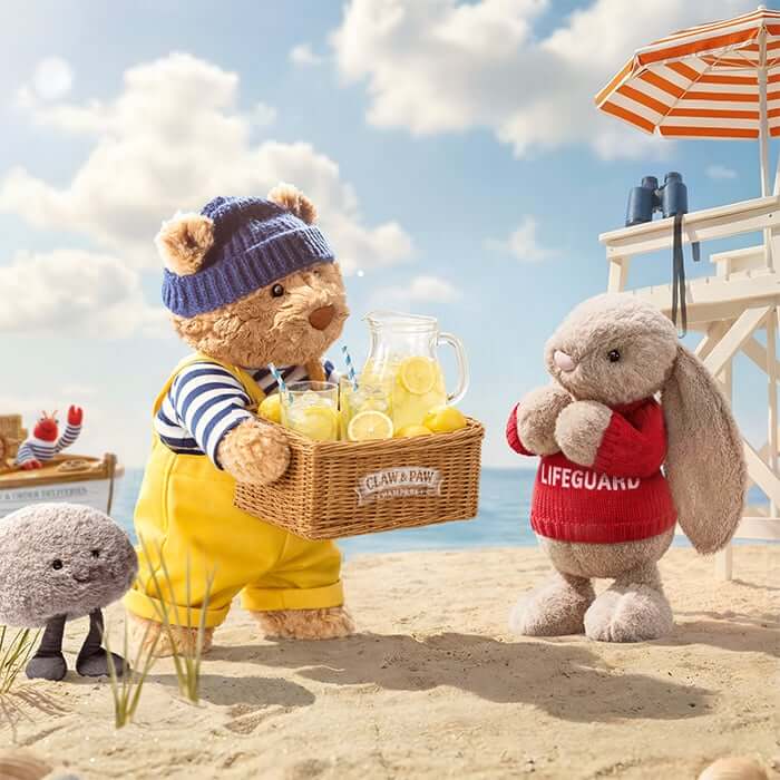 Bartholomew Bear carries a basket of lemonade while a lifeguard bunny stands on the beach nearby.