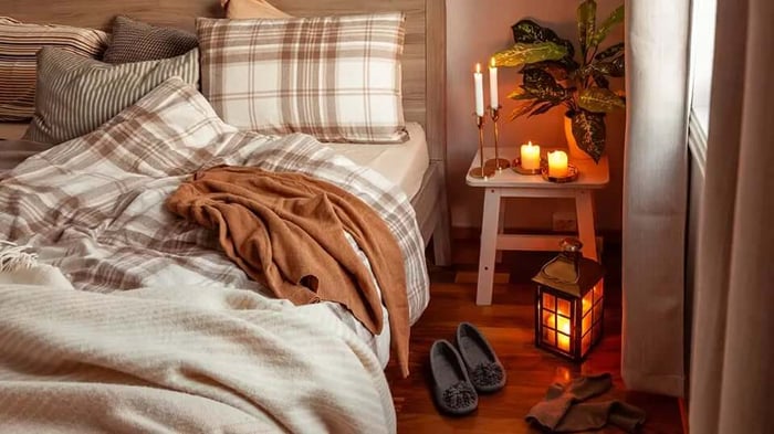 a cozy bed done in beige with a sweater and slippers waiting nearby