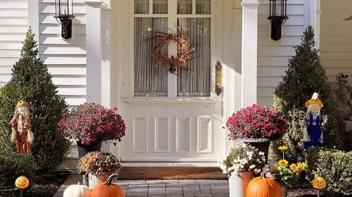 an antryway decorated by fall flowers and autumn scarecrows with a wreath on the door