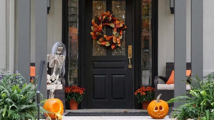 an entryway with a wreathe of fall leaves and spooky skeleton and pumpkin decorations