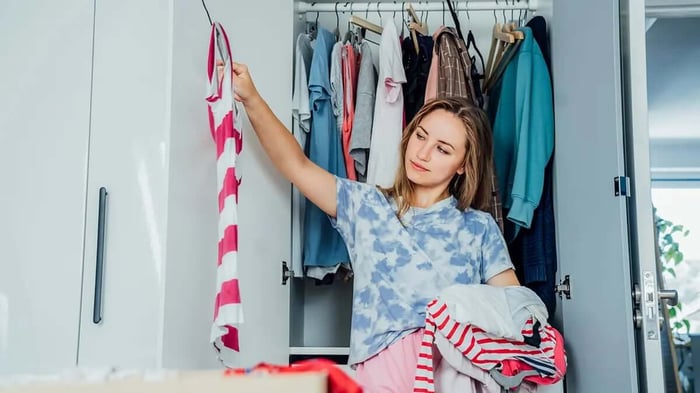 a woman with a closet behind her sorting clothes for her wardrobe swap