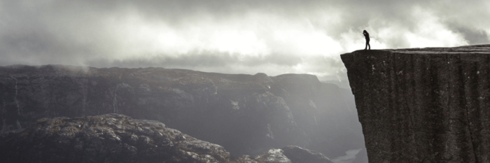 A black and white photo of a person looking hesitant or apprehensive, standing at the edge of a cliff or precipice, representing the boundary created by fear.