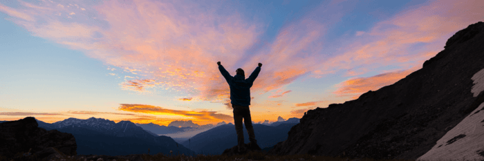 A person standing at a high viewpoint, overlooking a vast horizon or landscape, arms outstretched in triumph and acceptance of the future.