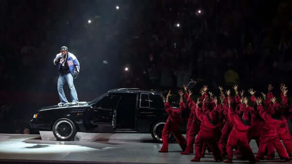 Kendrick standing on the hood of a car at the superbowl performance