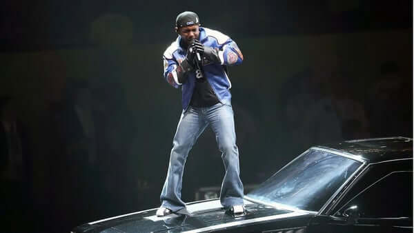 Up close of kendrick lamar standing on the hood of a muscle car