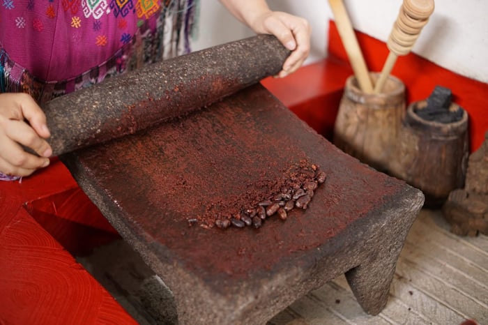 Guatemalan mayan woman making chocolate with traditional grinding stone