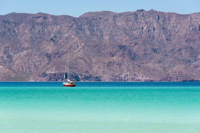 Mexico, Baja California Sur, Sea of Cortez, Loreto Bay. Lone sailboat on flat calm water with Sierra de la Giganta beyond