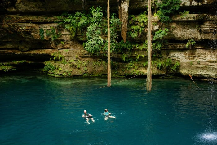 turquoise crystal clear water of San Lorenzo Oxman cenote lake with waterfall dripping from top of the opening in Yucatan Mexico